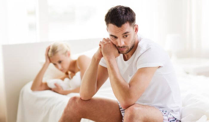 Concerned couple sitting apart on a bed while experiencing emotional stress related to fertility challenges.