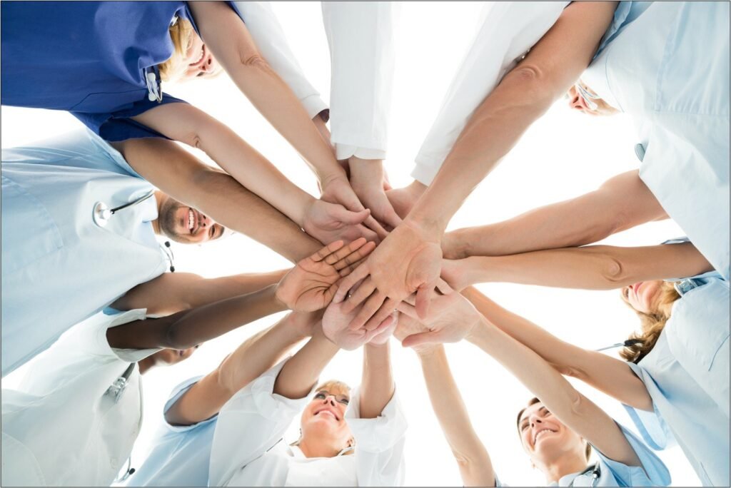 Ein medizinisches Team legt die Hände im Kreis übereinander, von unten fotografiert.